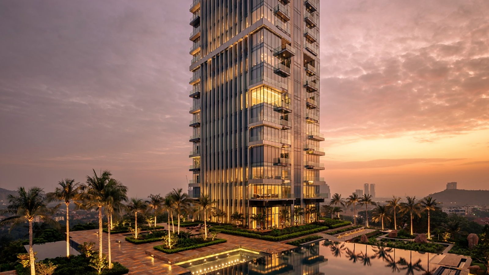 Luxury glass tower at sunset with landscape lighting and water reflection.