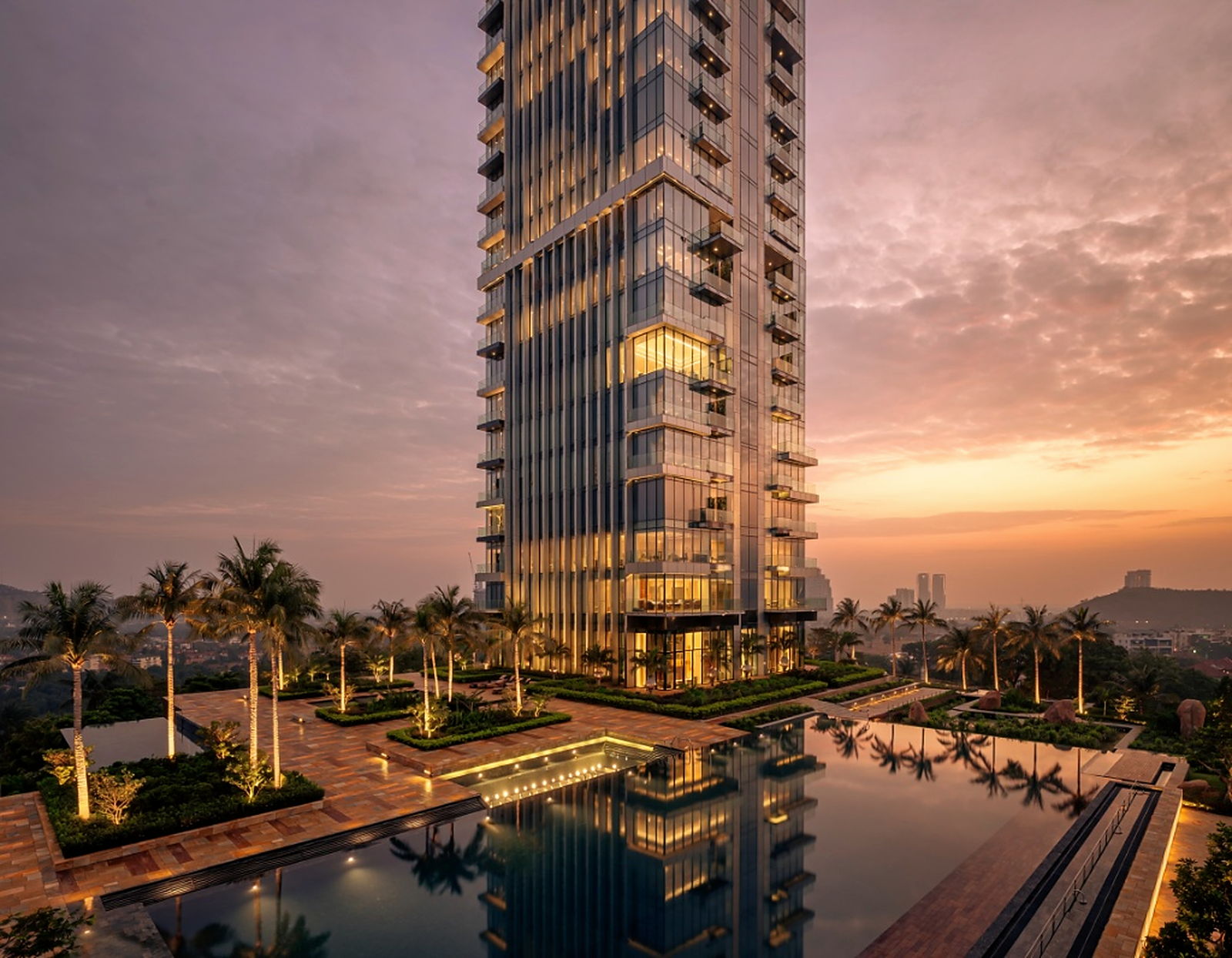 Luxury glass tower at sunset with landscape lighting and water reflection.